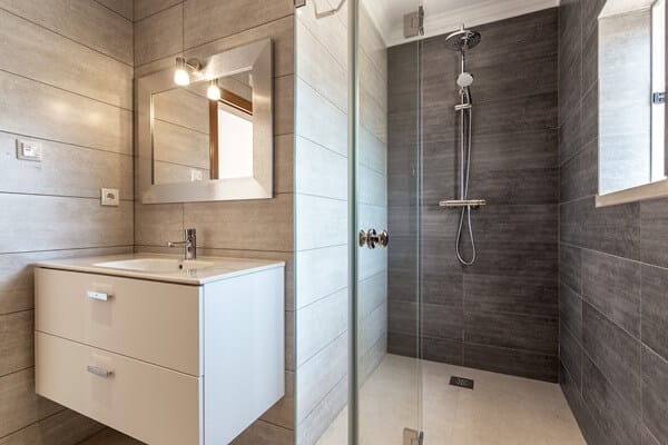 Photo de l'intérieur d'une salle de bain rénovée, avec une douche à l'italienne, carrelage mural gris, colonne de douche et meuble vasque mural à Le Petit Quevilly